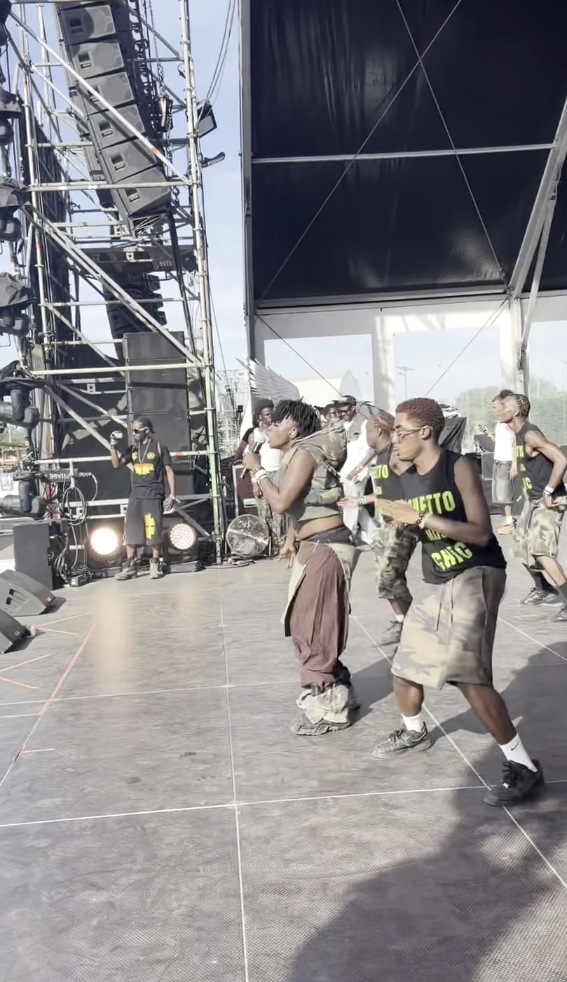 Ezek at the mic on the Yardland stage, dancers moving behind her
