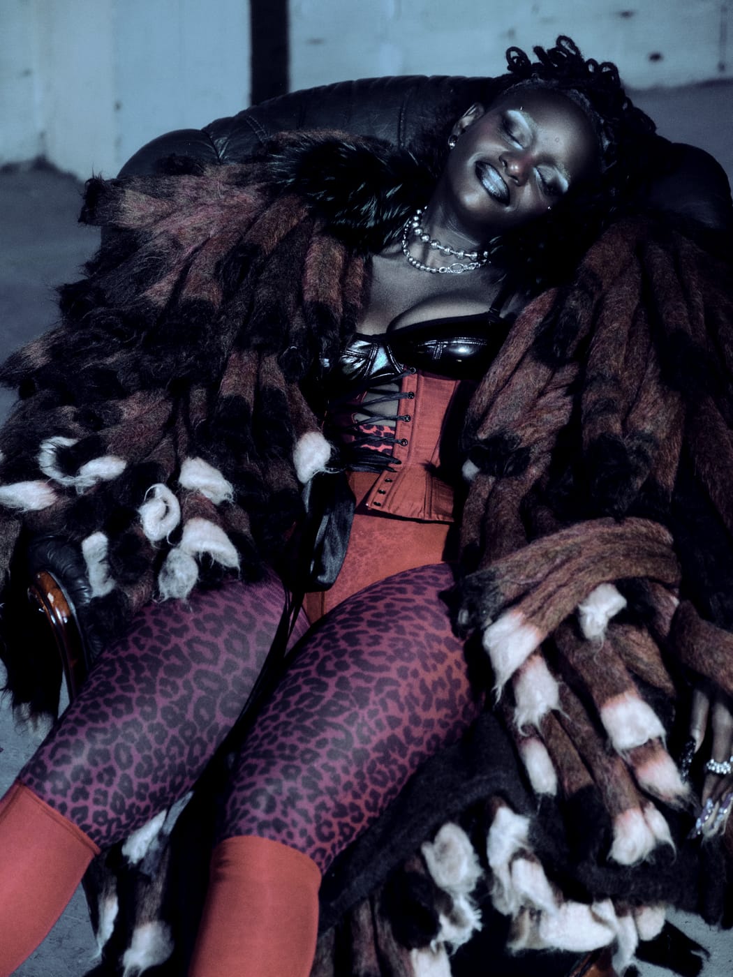 Ezek lying back in the fur, leather corset top and red lacing, chains at her neck