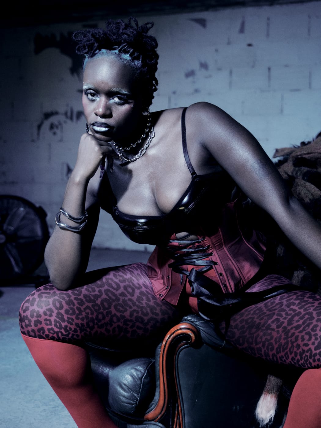 Ezek close, chin on fist, in the fur and red corset, blue light