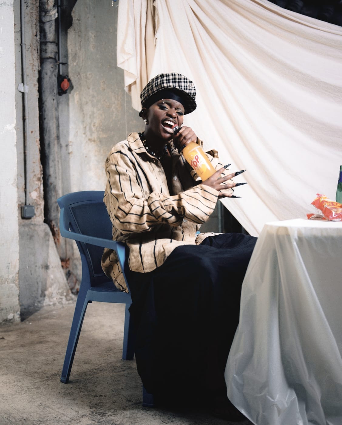 Ezek at the table in the beret, drinking a Fanta, long black press-on nails