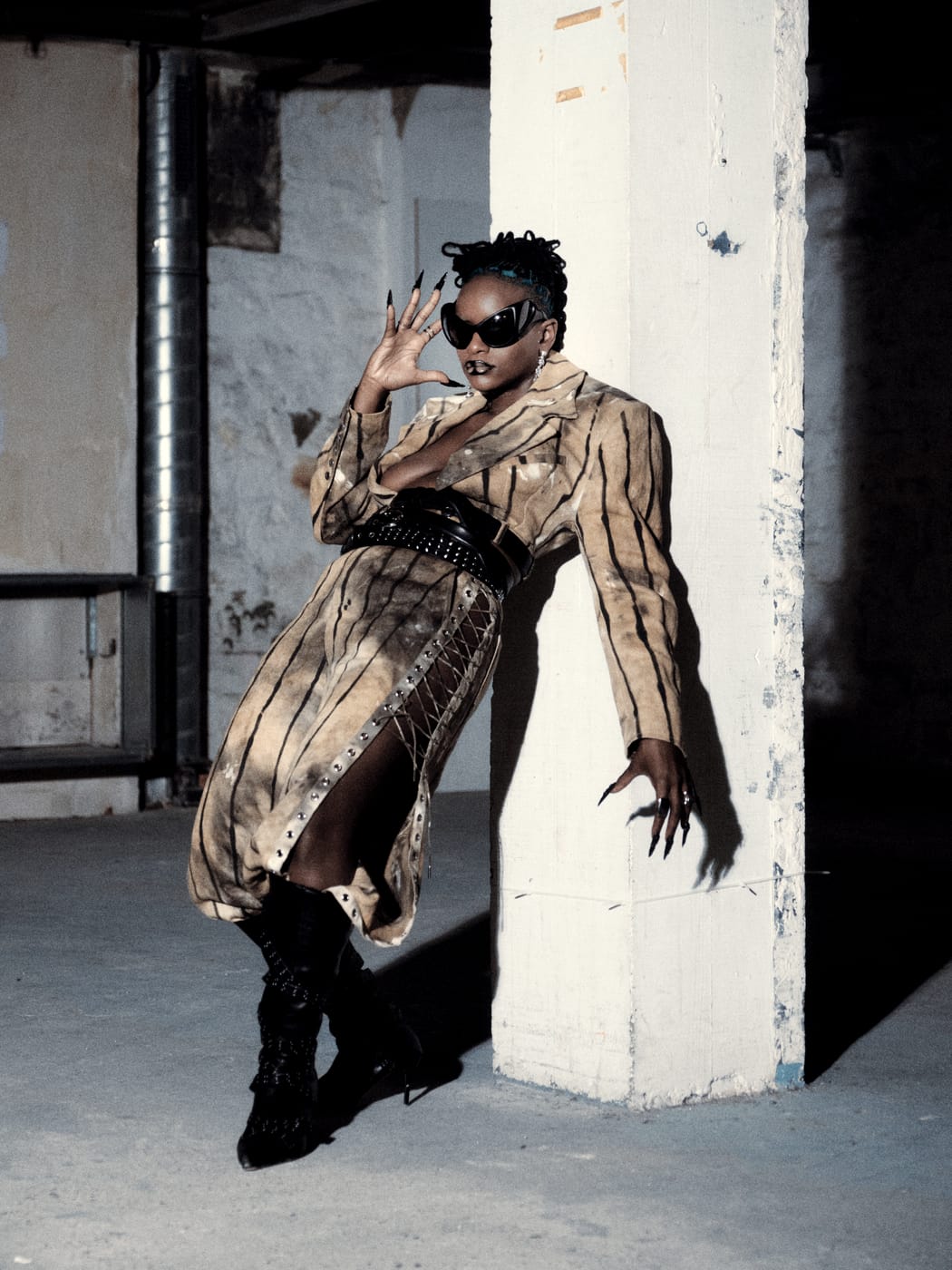 Ezek leaning at the pillar in the striped coat, claw nails raised, boots crossed