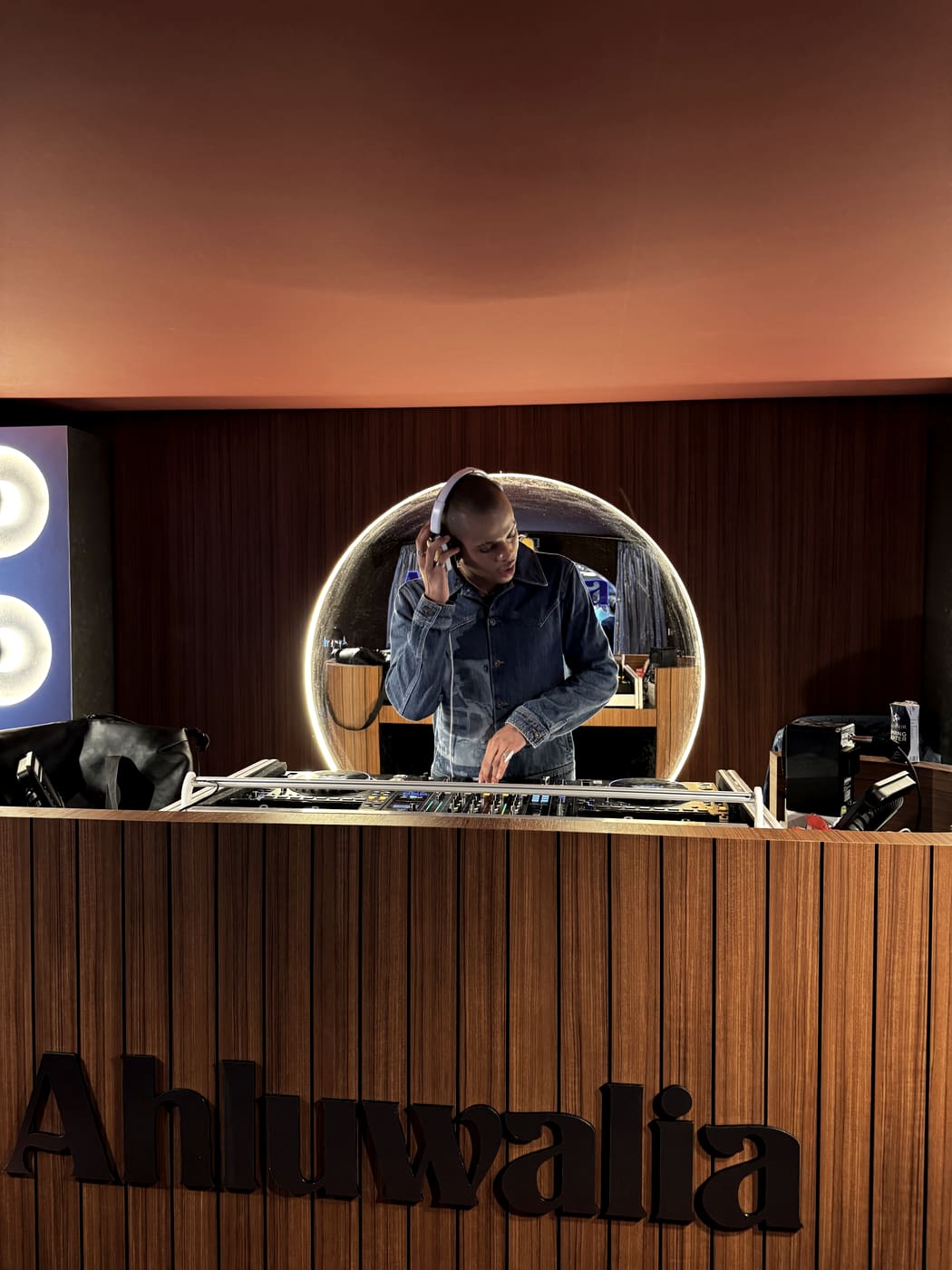 Oluwa behind the decks of the listening room, one headphone held to his ear, the Ahluwalia name across the timber front