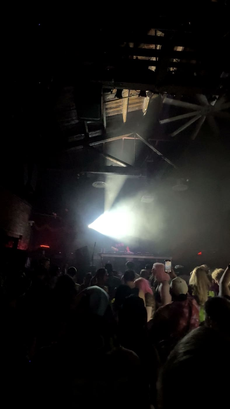A single spotlight cone over the crowd at Brooklyn Bowl, timber rafters above